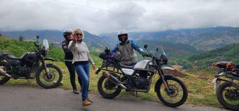 Smiling tour participants posing with their motorbikes against a backdrop of misty Vietnamese mountains.